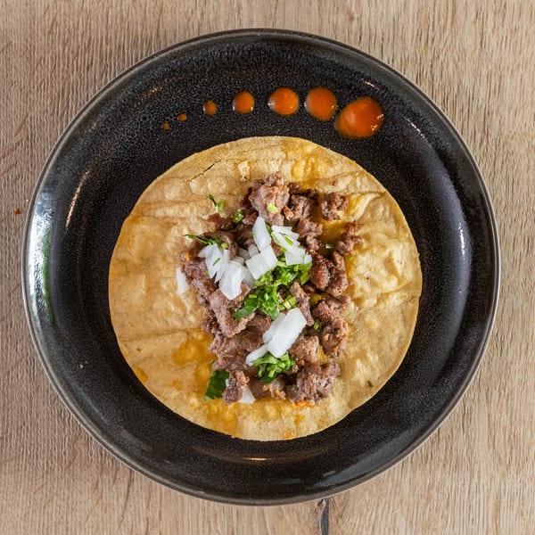 Overhead view of a single taco with meat, onions, and cilantro on a dark plate with hot sauce.