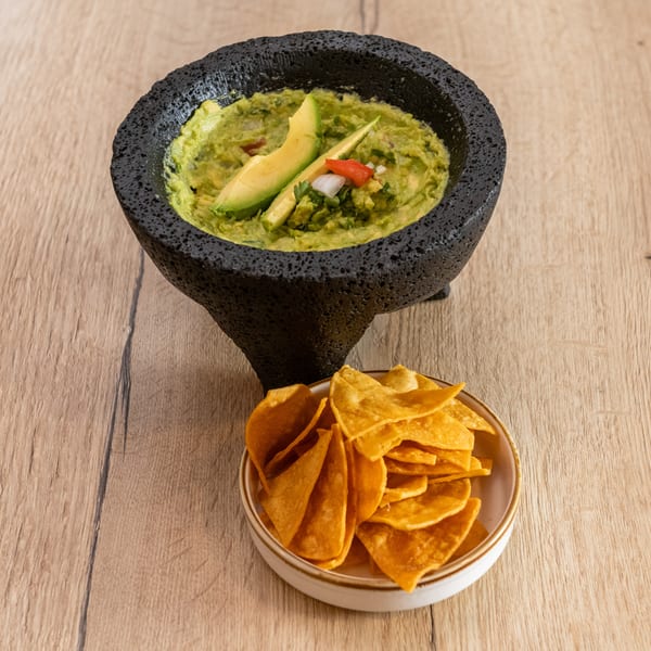 Guacamole in a molcajete with avocado slices, onions, and cilantro, served with tortilla chips.