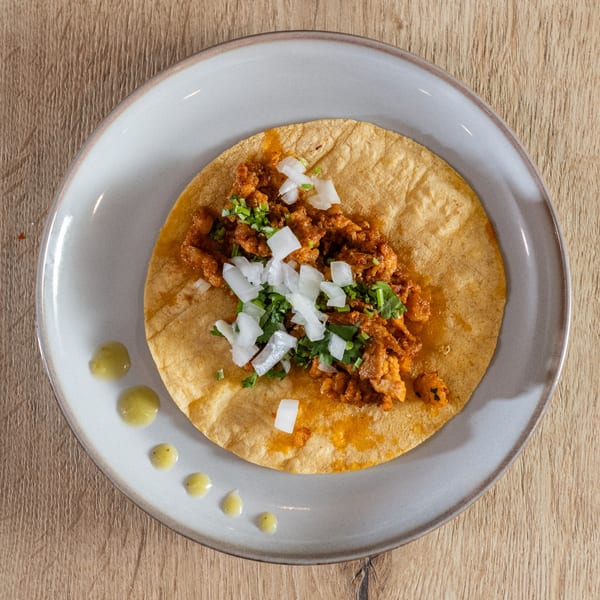 Overhead view of a single al pastor taco with onions and cilantro on a gray plate.