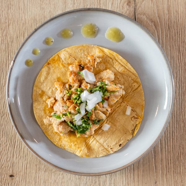 Overhead view of a single taco with meat, chopped onions, and cilantro on a white plate.
