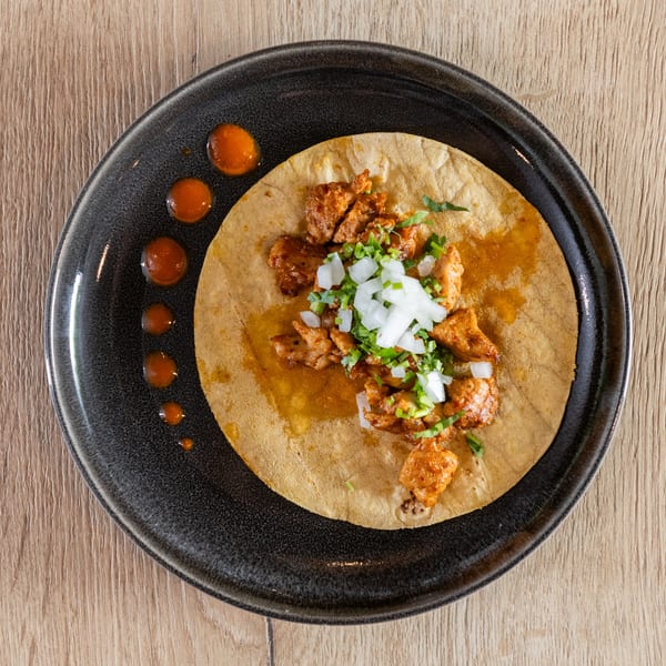 Overhead view of a single taco with meat, onions, and cilantro on a dark plate with sauce dots.