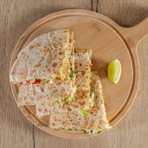 Four quesadilla slices filled with lettuce, tomato, and cheese, served with a lime wedge on a wooden board.